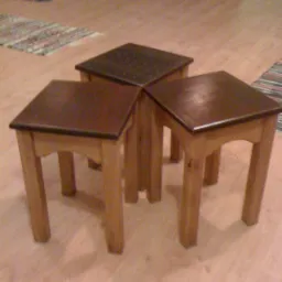 Trzy drewniane stoliki kawowe z ciemnymi blatami, ustawione obok siebie na podłodze w pomieszczeniu.